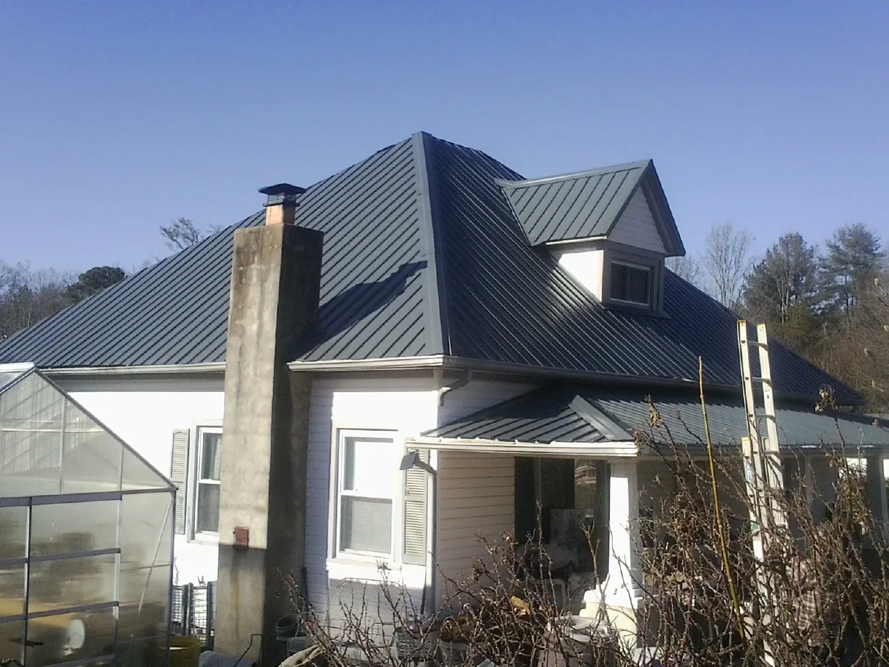 Dark blue standing seam metal roof on a white farmhouse with dormer — Slate & Tile Roof Repair by Roofing Brothers in River Edge