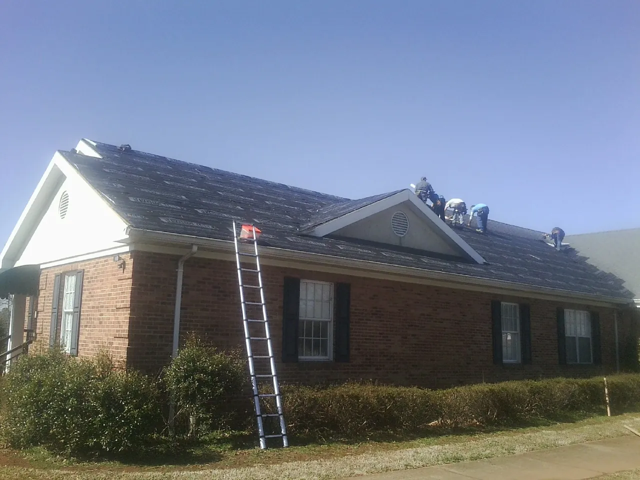 Crew tearing shingles off a brick ranch roof with a ladder set — Emergency Roof Repair work by our crew in River Edge