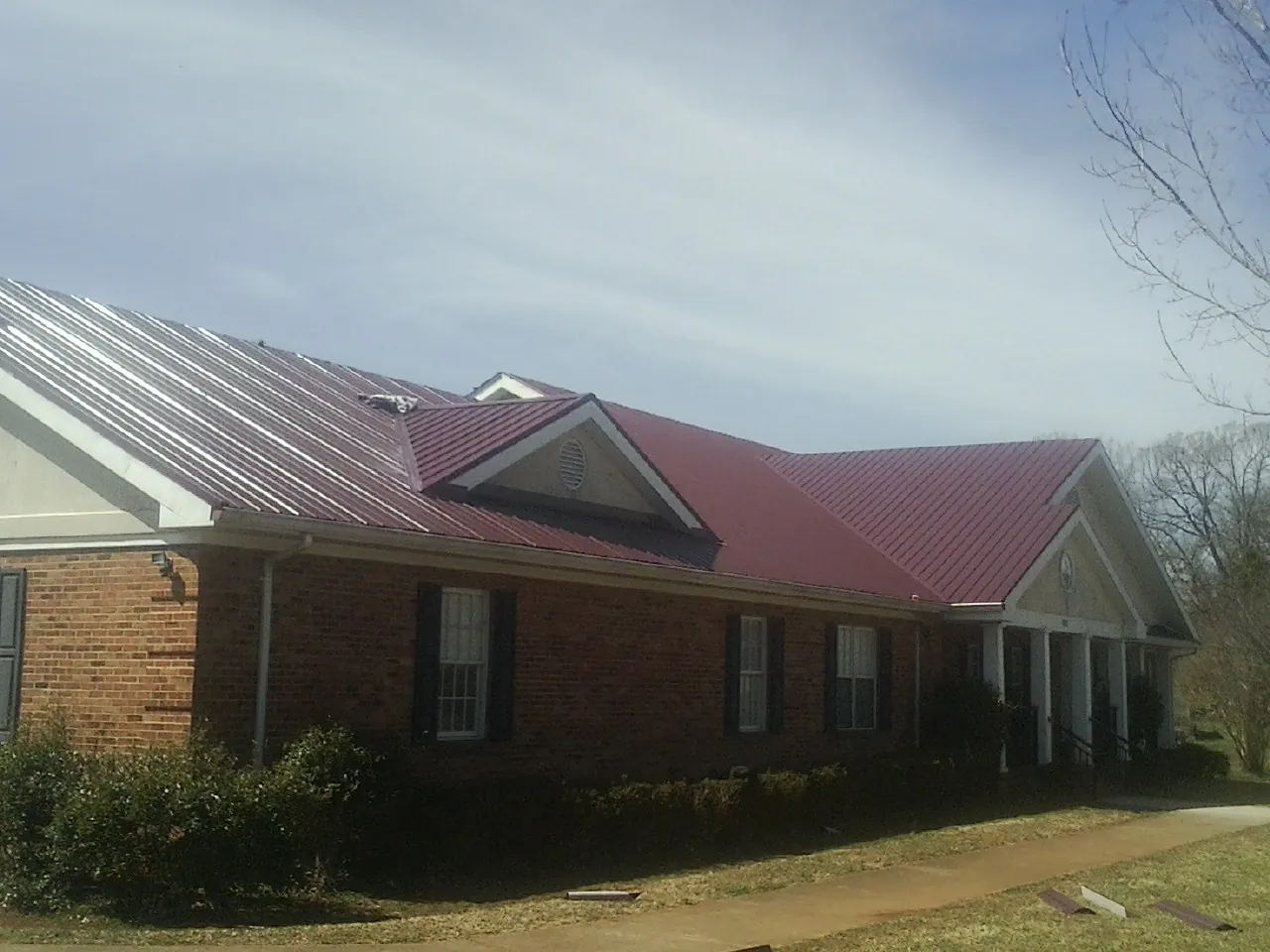 Red metal roof with gabled entries on a long brick building, from a Hail Damage Roof Repair job in River Edge
