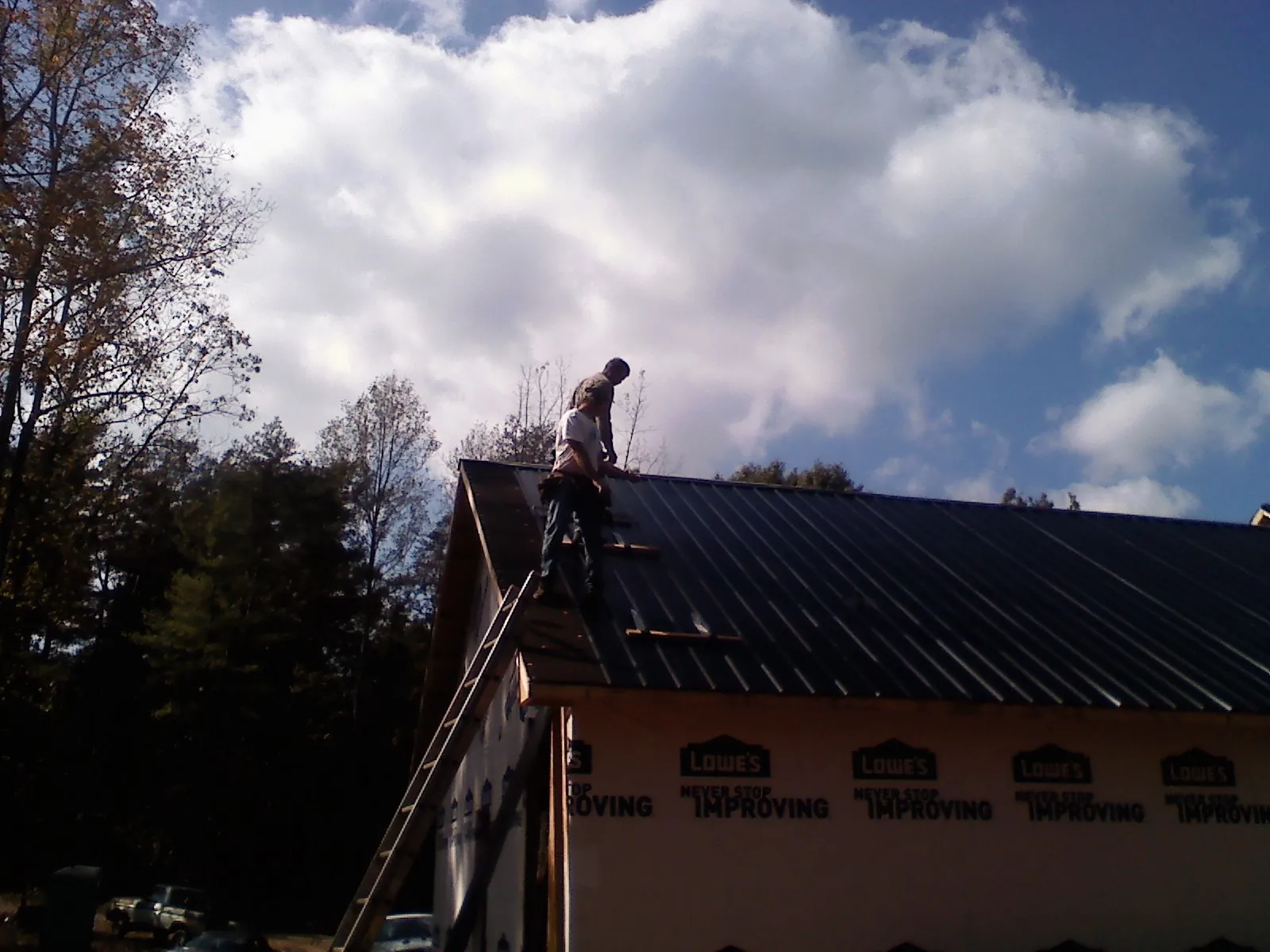 Roofer fastening dark metal panels high against a cloudy sky, from a Roof Inspection job in River Edge