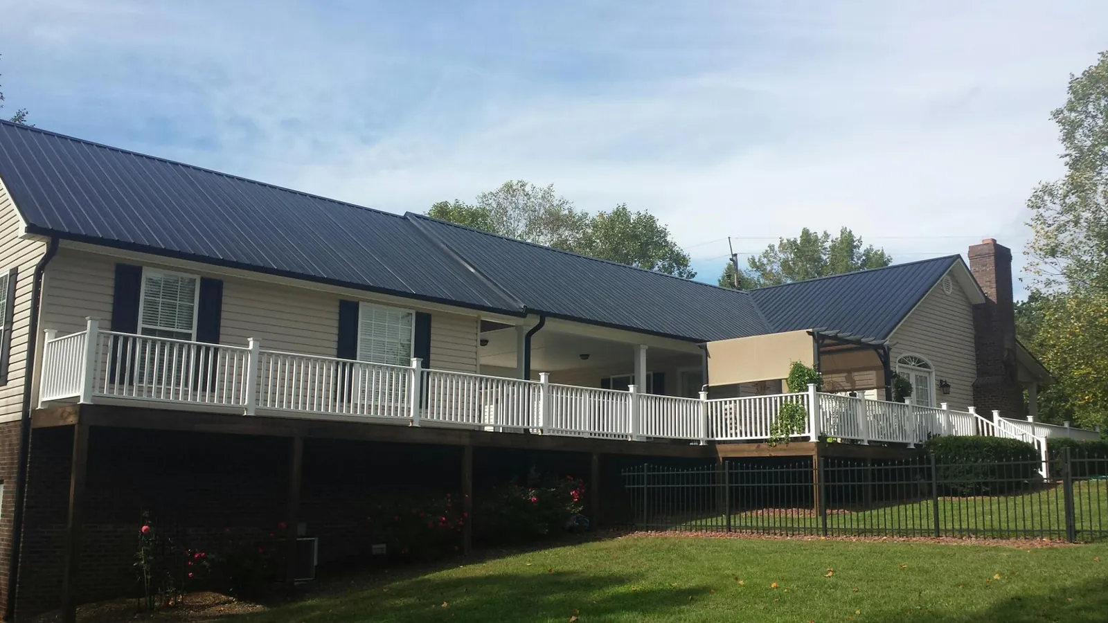 Black metal roof above a long white railed deck on a hillside home in River Edge