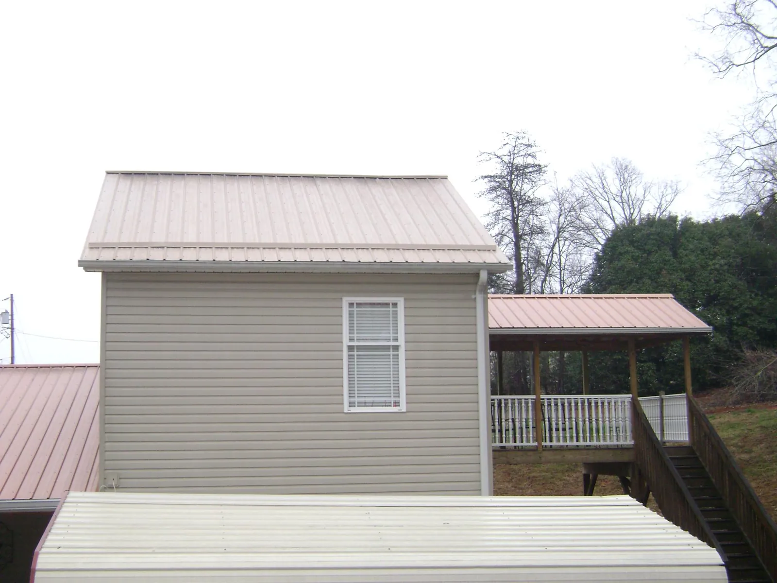 Tan metal roofs on a two story addition and attached porch, from a Roof Replacement job in River Edge